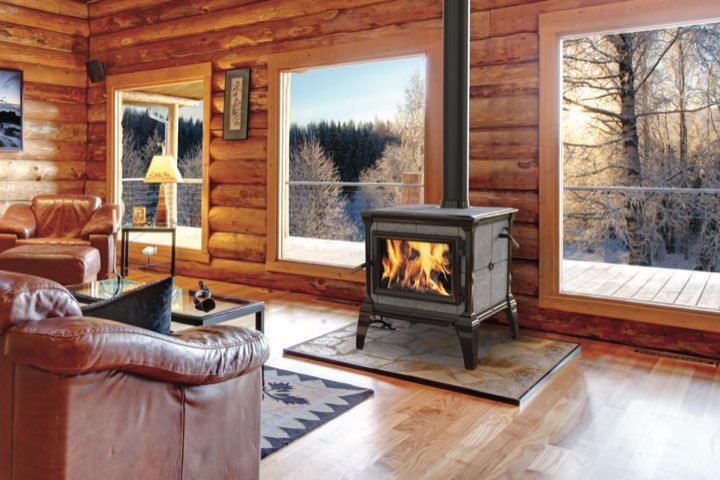 Hearthstone soapstone stove burning in a log cabin living room with winter views