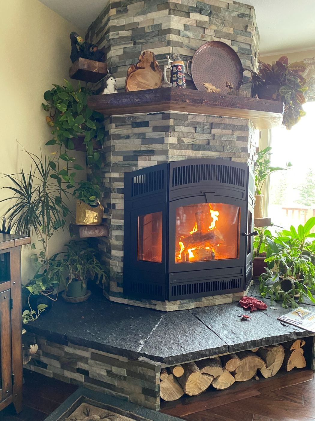 Wood fireplace with a roaring fire in a custom stacked-stone hearth, firewood stored below